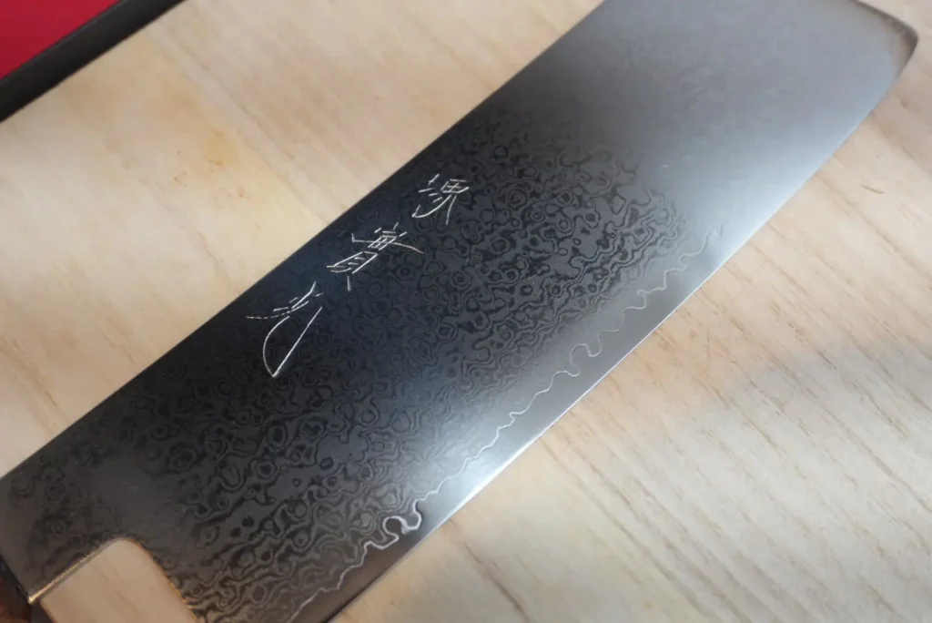 JIKKO Nakiri blade showing 33-layer Damascus texture and hand-engraved kanji, in daily use